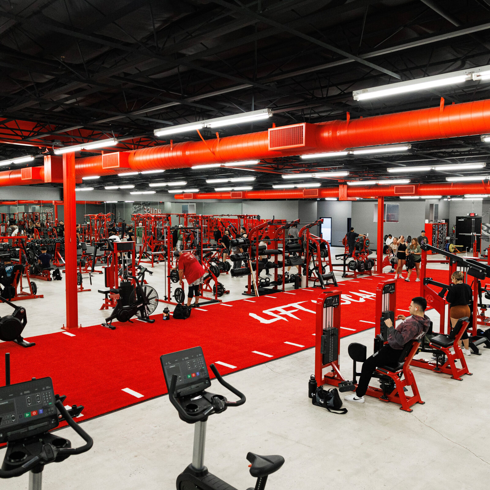Elevated view of the House of Gains gym floor — custom red machines, red ductwork and the red turf runway with white dash lines