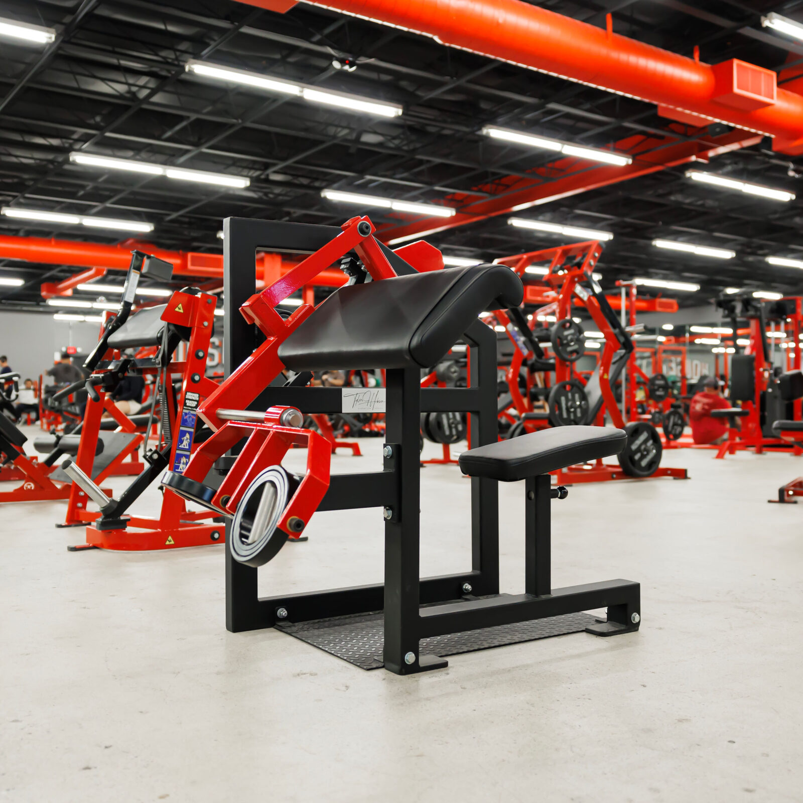 Close-up of a custom red and black plate-loaded machine on the gym floor