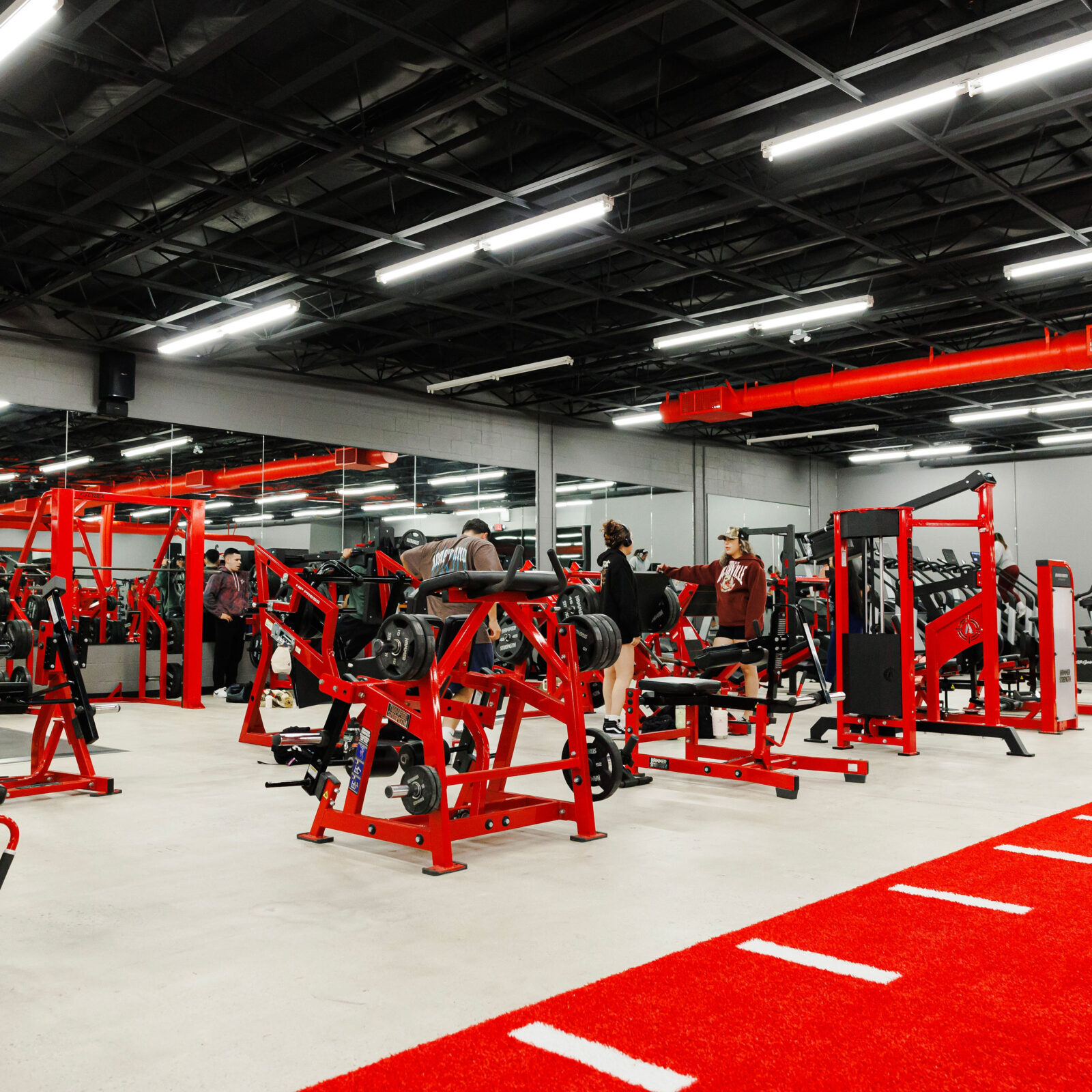 Members training across the busy gym floor with red machines and turf