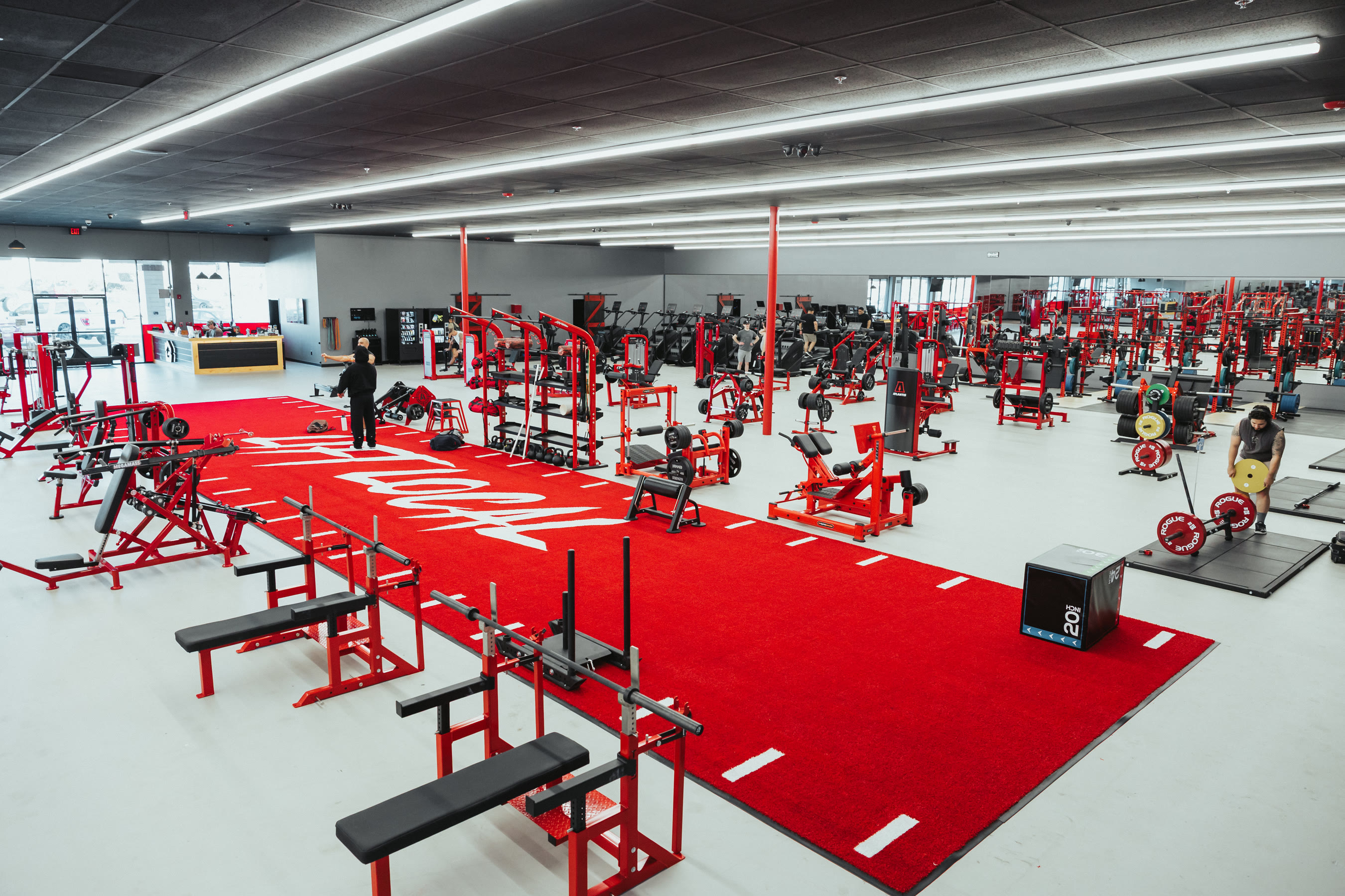 The Camarillo floor — red turf runway with the House of Gains logo, machines and racks down both sides