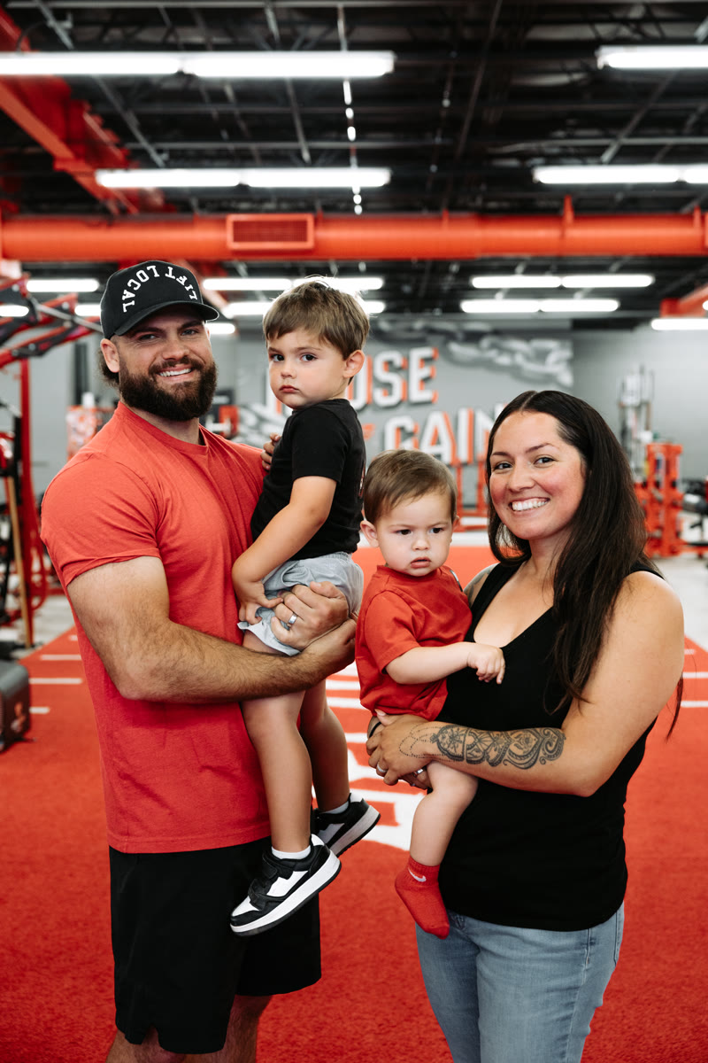 David and Victoria with their two kids in their arms, on the red turf runway of the House of Gains floor