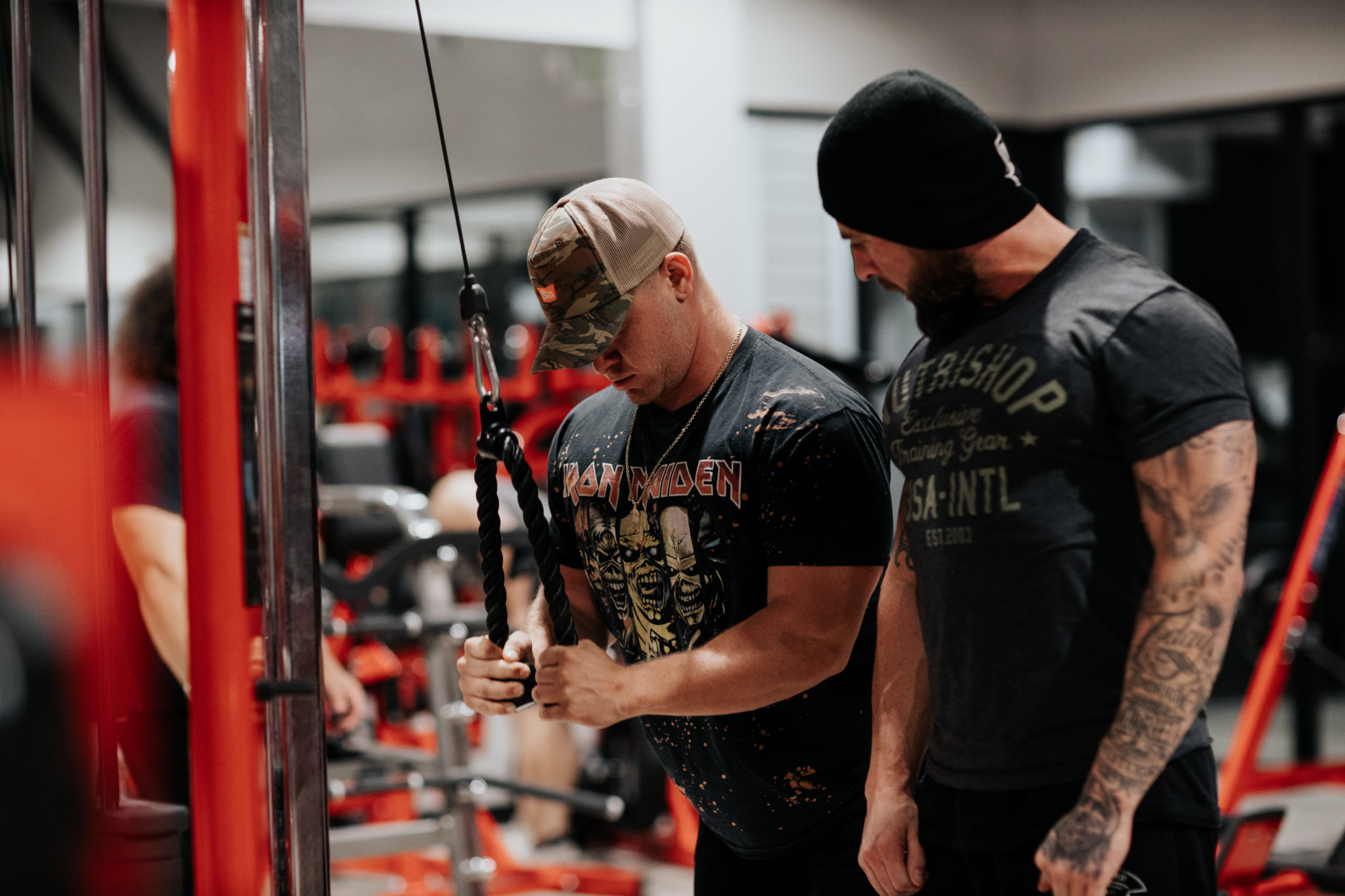 Two lifters working a cable machine — coaching on the House of Gains floor